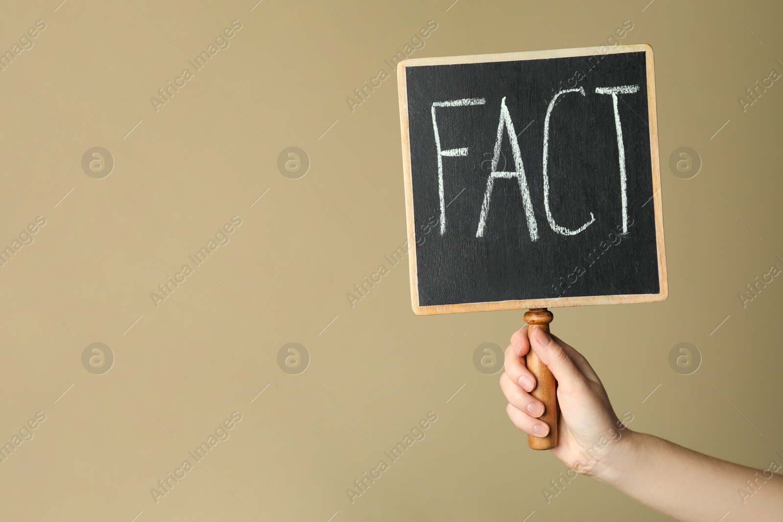 Photo of Woman holding small chalkboard with word FACT near beige wall, closeup. Space for text