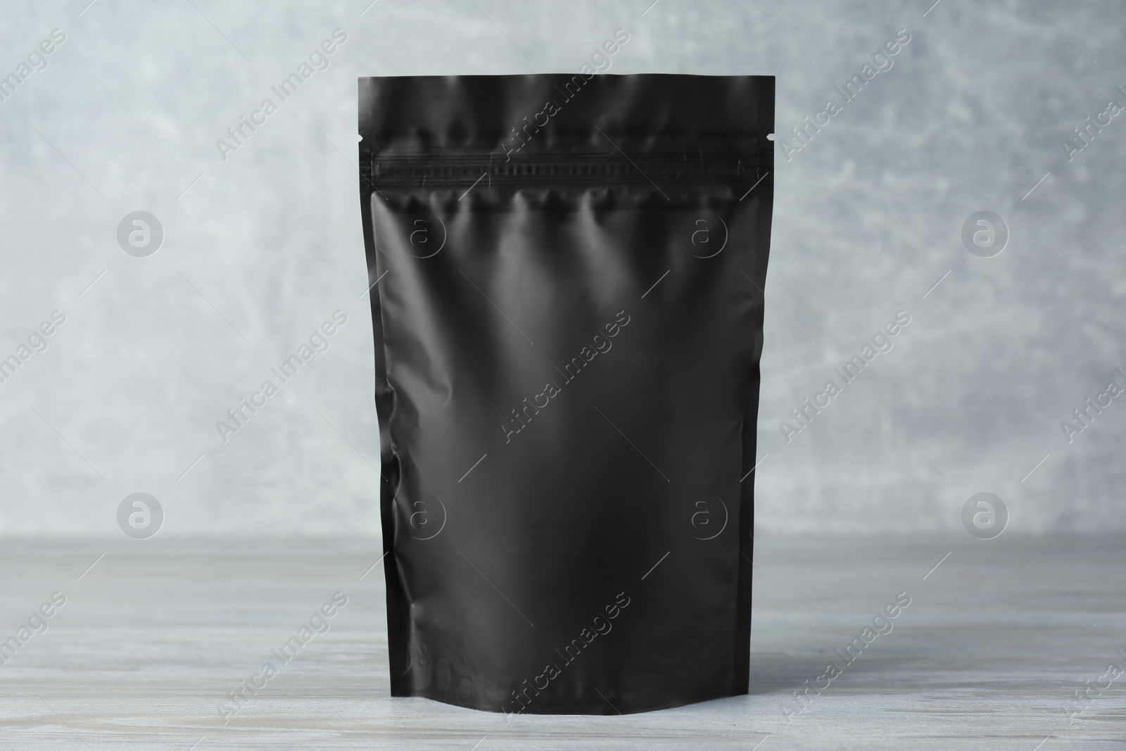 Photo of One blank foil package on wooden table against light grey background