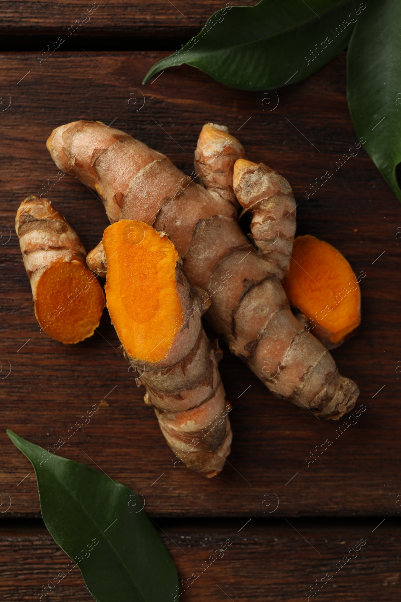 Photo of Fresh turmeric roots and leaves on wooden table, flat lay
