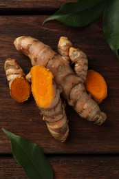 Fresh turmeric roots and leaves on wooden table, flat lay