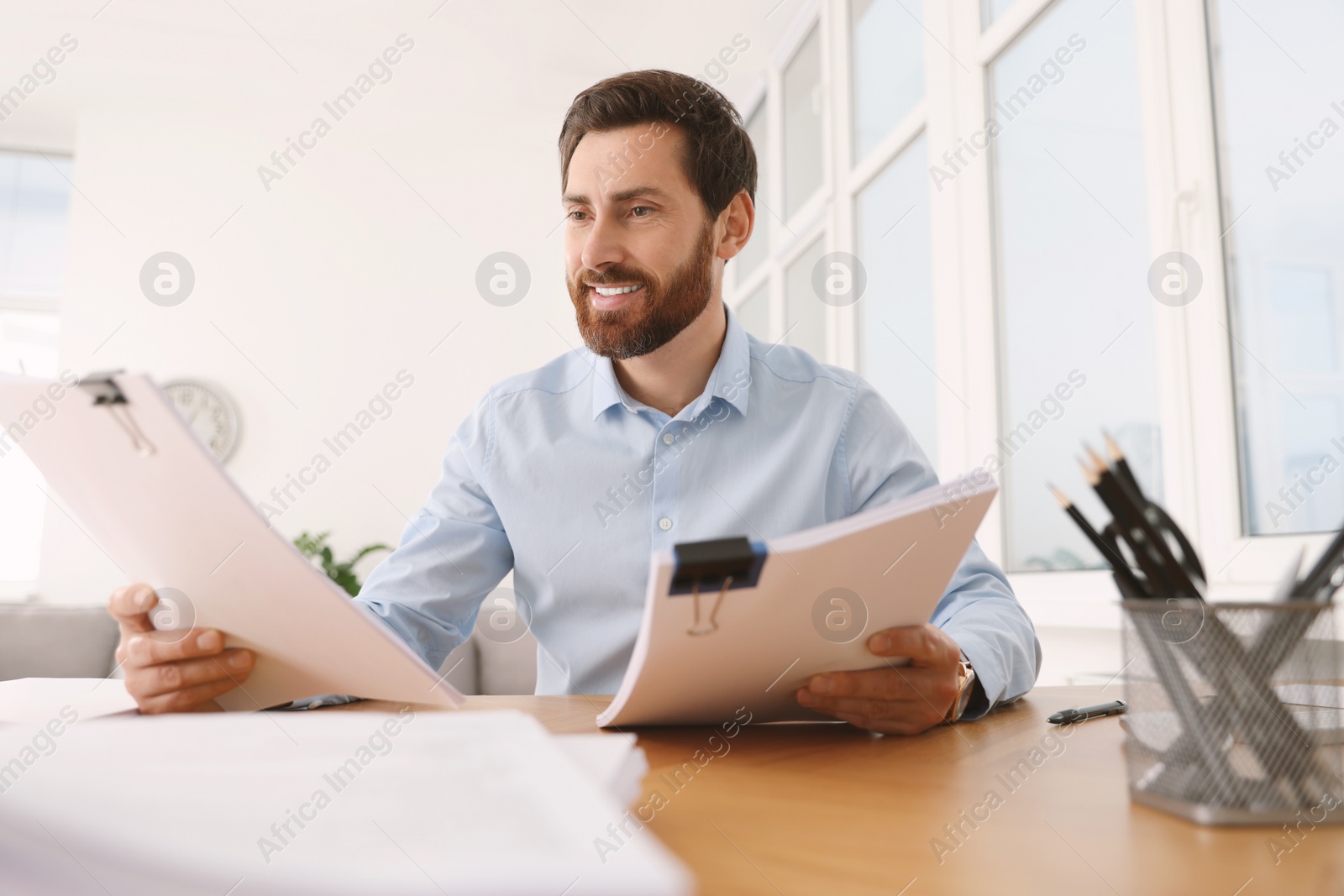 Photo of Happy businessman working with documents at wooden table in office