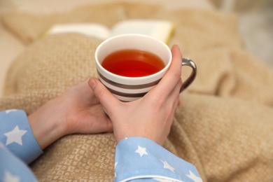 Photo of Woman with cup of tea and beige plaid indoors, closeup