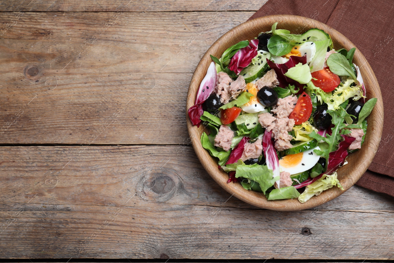 Photo of Bowl of delicious salad with canned tuna and vegetables on wooden table, flat lay. Space for text