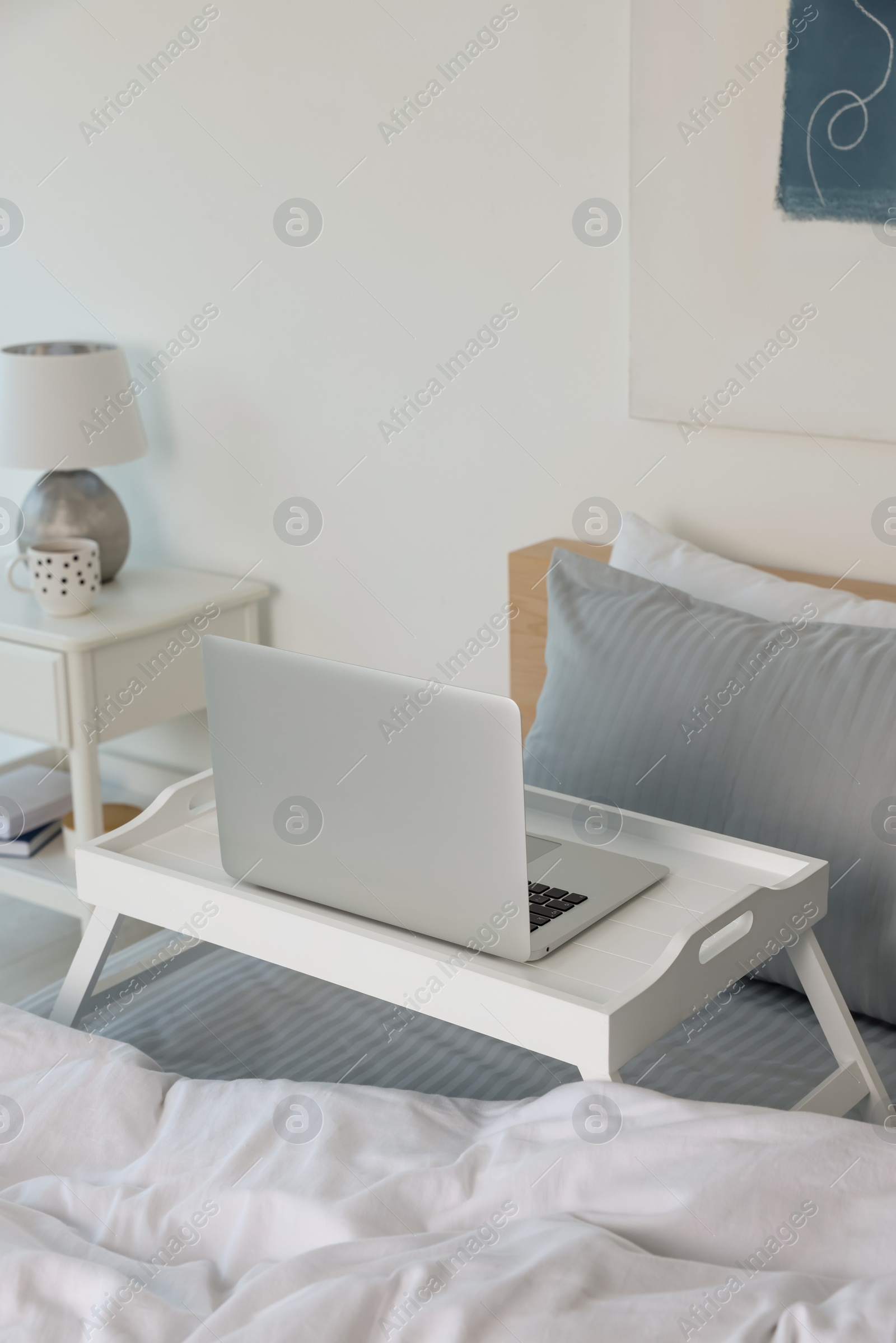 Photo of White tray table with laptop on bed indoors