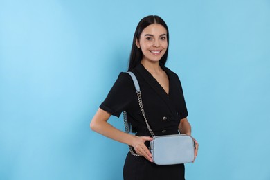 Beautiful young woman with stylish bag on light blue background