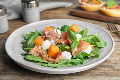 Photo of Fresh melon with prosciutto, mozzarella and arugula on wooden table