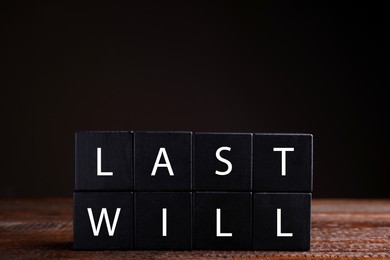 Photo of Black cubes with words Last Will on wooden table against dark background