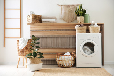 Photo of Modern washing machine and plants in laundry room interior