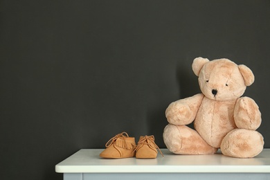 Photo of Teddy bear with bootees for baby room interior on table near black wall