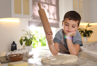 Photo of Cute little boy with dough and rolling pin at table in kitchen. Cooking pastry