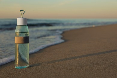 Photo of Glass bottle with water on wet sand near sea at sunset. Space for text