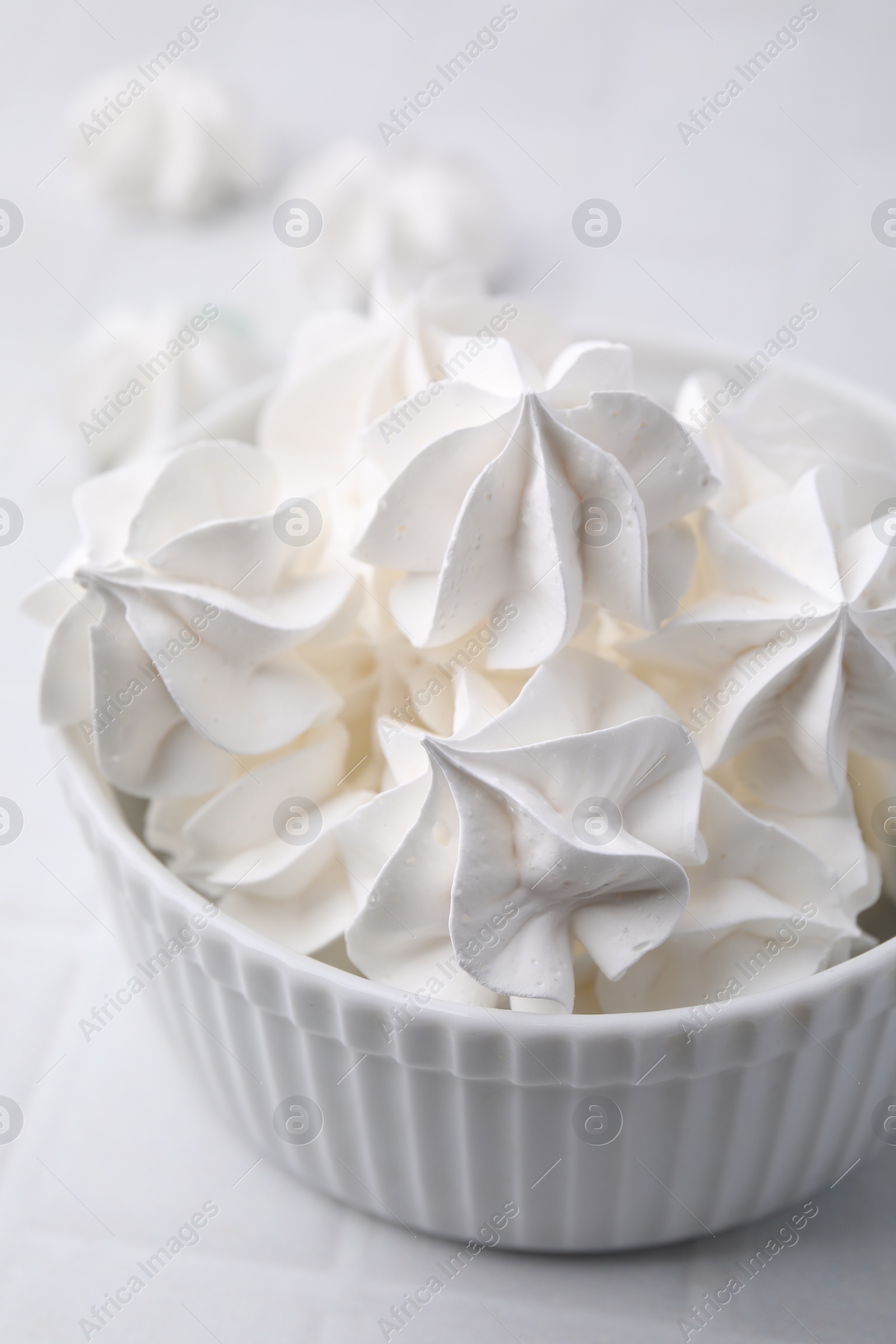 Photo of Delicious meringue cookies in bowl on white table, closeup