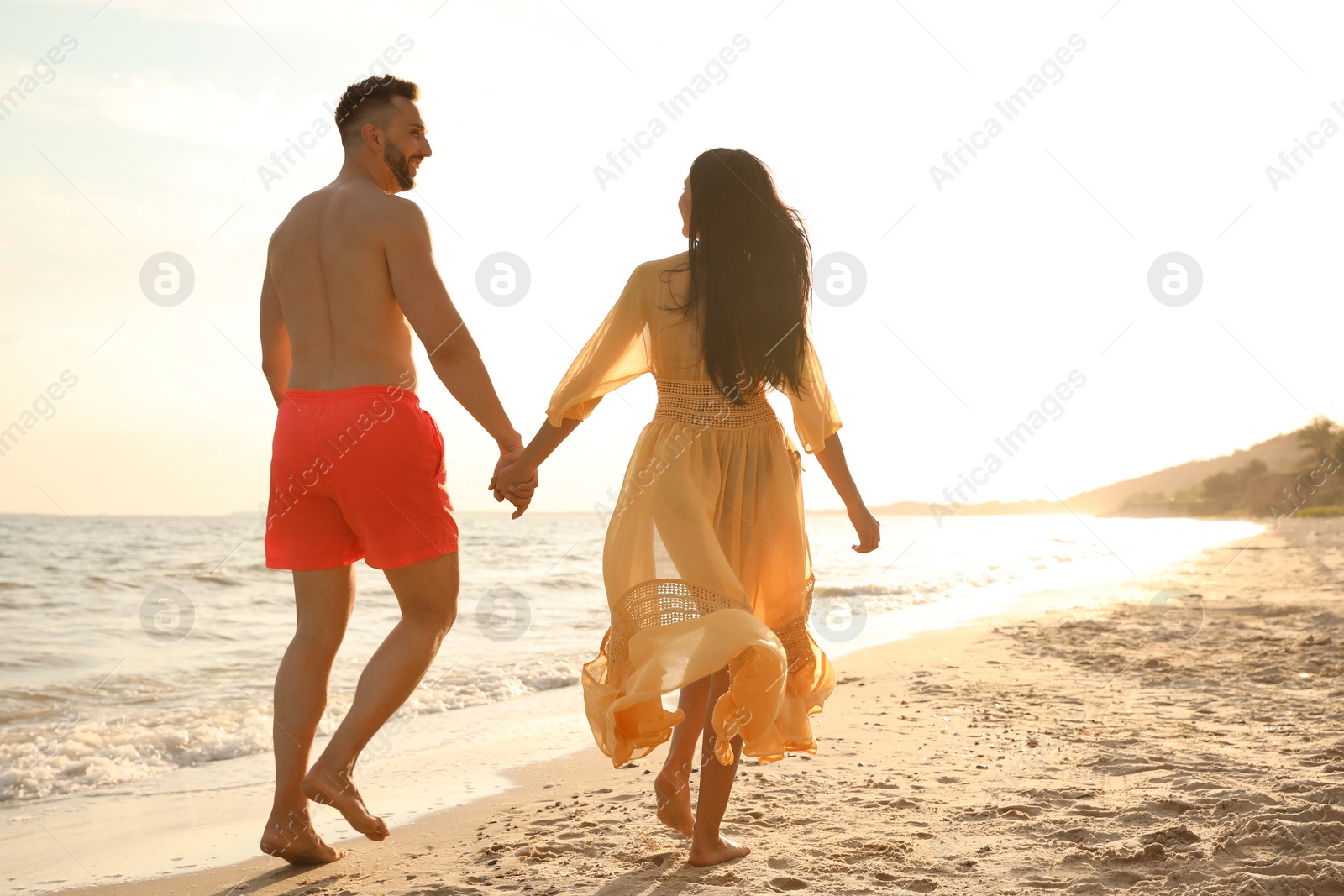 Photo of Happy couple walking together on beach at sunset, back view