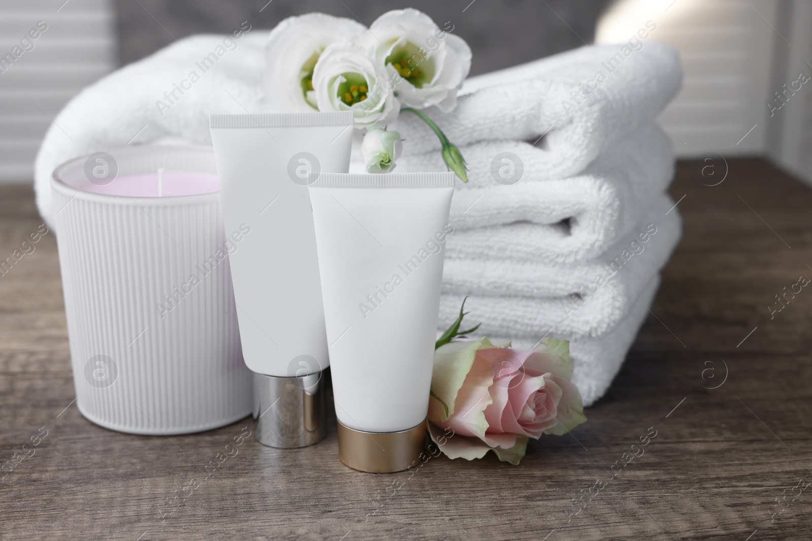 Photo of Cosmetic products, scented candle and folded towels with flowers on wooden table indoors