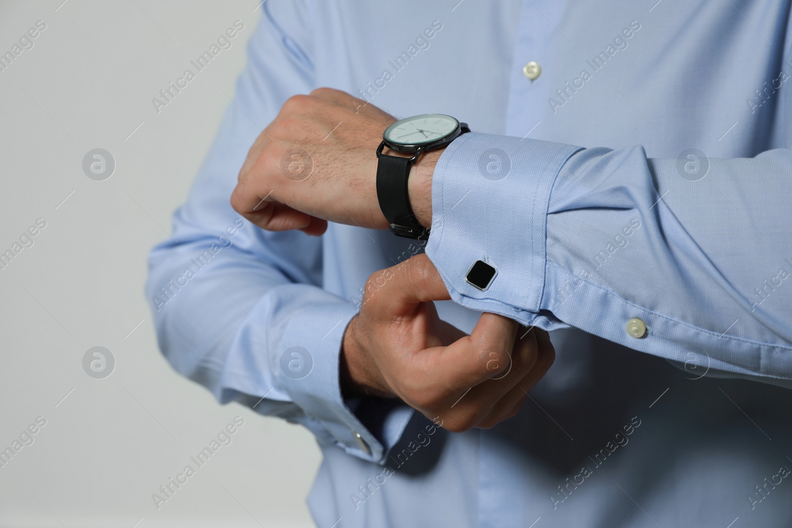 Photo of Stylish man putting on cufflink against grey background, closeup