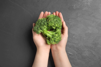 Photo of Woman holding fresh green broccoli over black table, top view