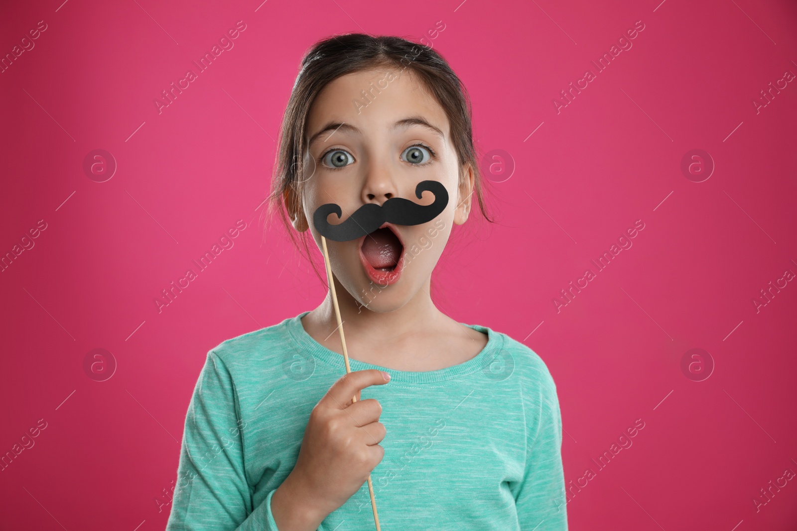 Photo of Cute little girl with fake mustache on pink background