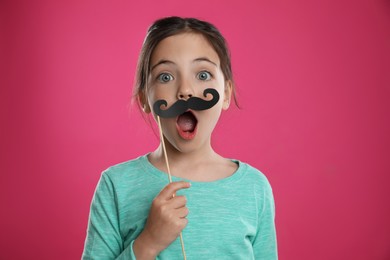 Cute little girl with fake mustache on pink background