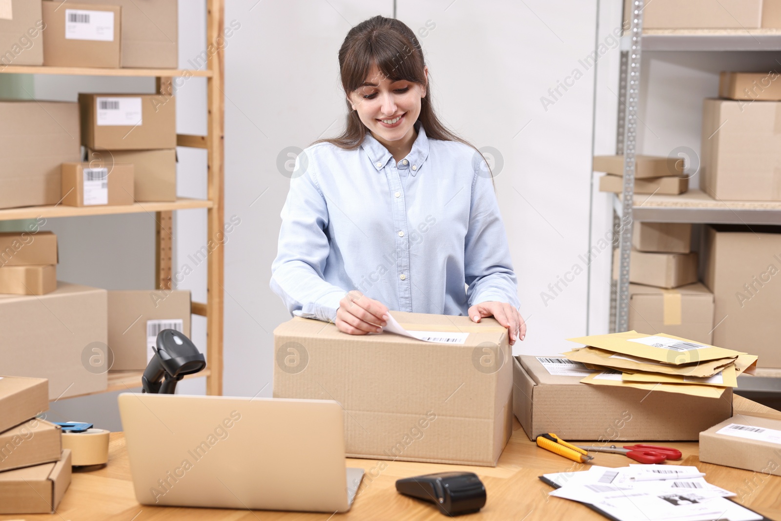 Photo of Parcel packing. Post office worker sticking barcode on box at wooden table indoors