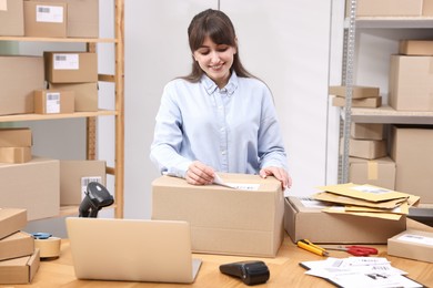 Parcel packing. Post office worker sticking barcode on box at wooden table indoors