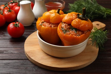 Photo of Tasty stuffed peppers in bowl on wooden table, closeup