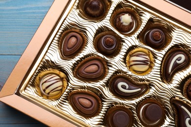 Photo of Box of delicious chocolate candies on light blue wooden table, top view