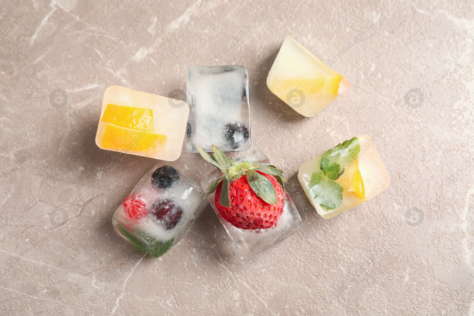 Photo of Ice cubes with different berries and mint on grey table, flat lay