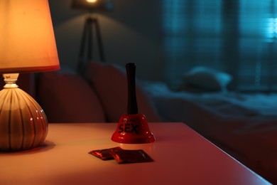 Photo of Ring for sex bell and condoms on bedside table in bedroom at night