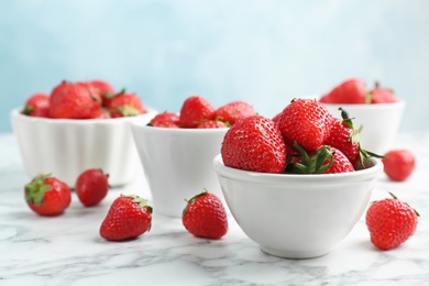 Photo of Bowls with ripe red strawberries on marble table