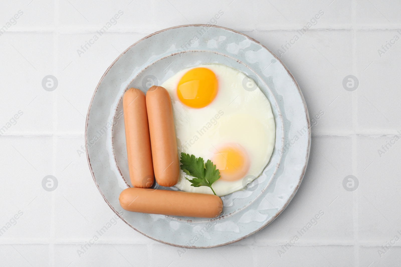 Photo of Delicious boiled sausages, fried eggs and parsley on white tiled table, top view