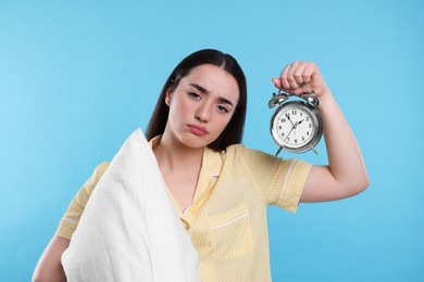 Photo of Tired young woman with pillow and alarm clock on light blue background. Insomnia problem