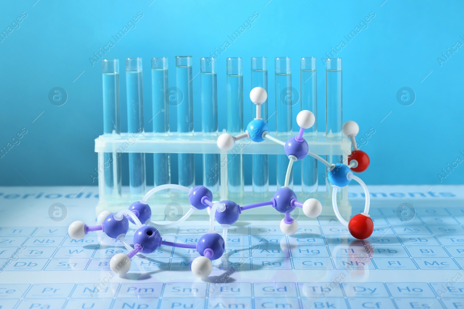 Photo of Molecular model and test tubes on periodic table against light blue background