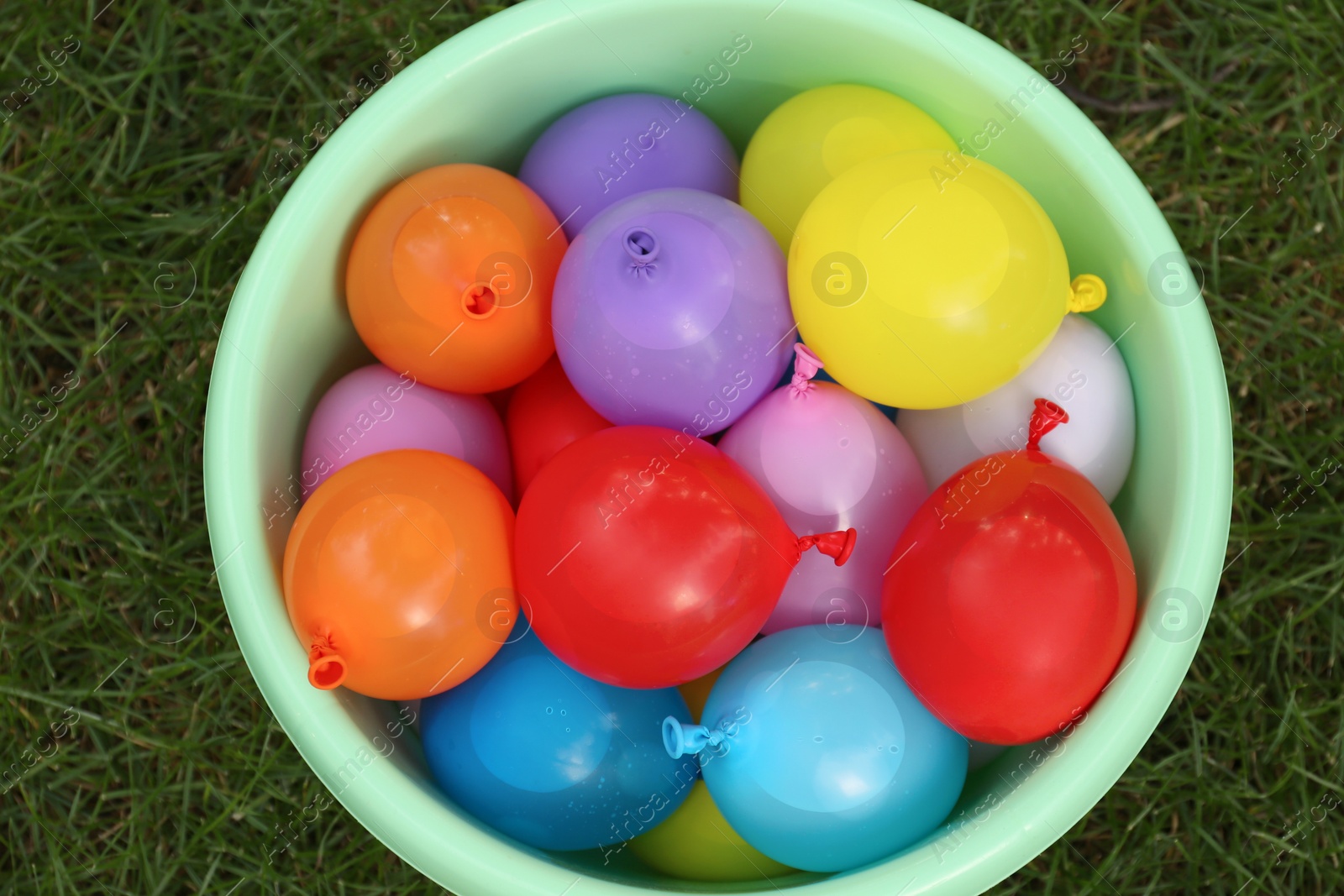 Photo of Basin full of water bombs on green grass, top view