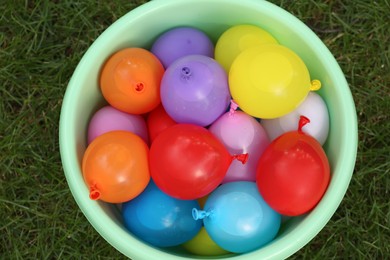 Basin full of water bombs on green grass, top view