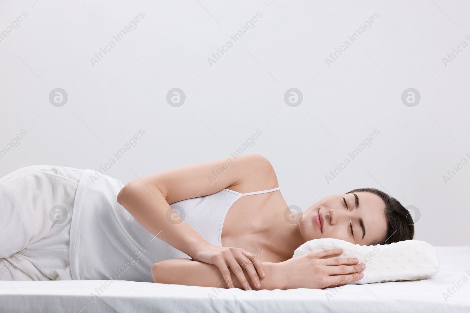 Photo of Woman sleeping on orthopedic pillow against light grey background, space for text