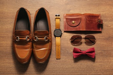 Stylish red bow tie, brown shoes, wallet and accessories on wooden background, flat lay