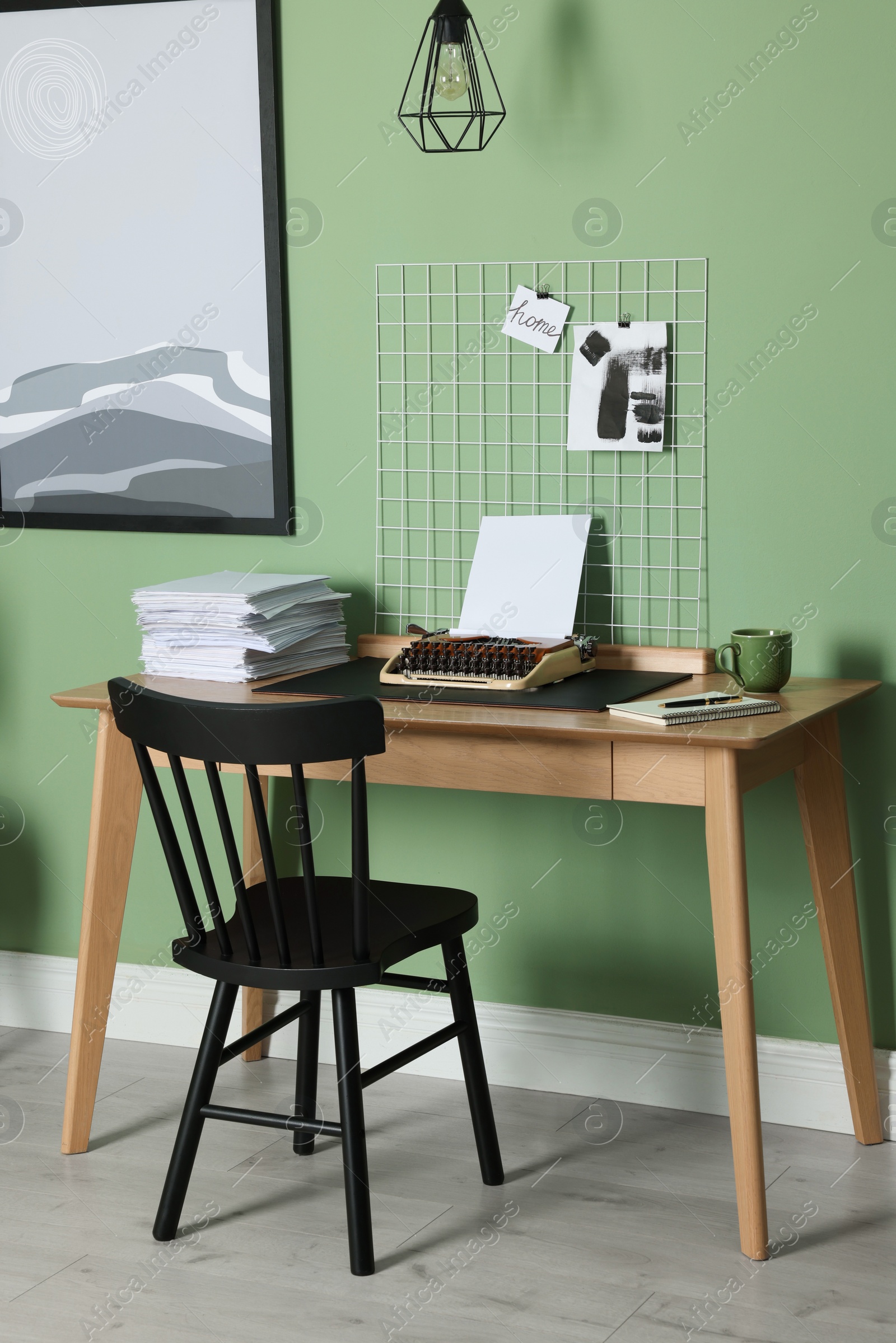 Photo of Typewriter, stack of papers and mood board on wooden table near pale green wall. Writer's workplace