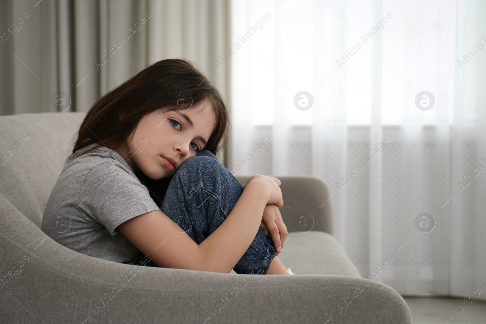 Photo of Sad little girl sitting on sofa indoors, space for text