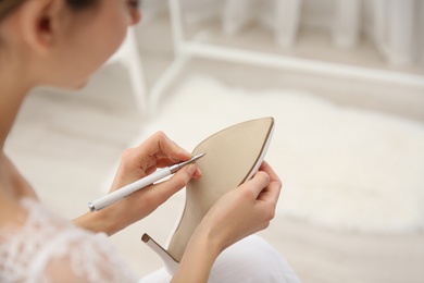 Young bride writing on her shoe indoors, closeup. Wedding superstition