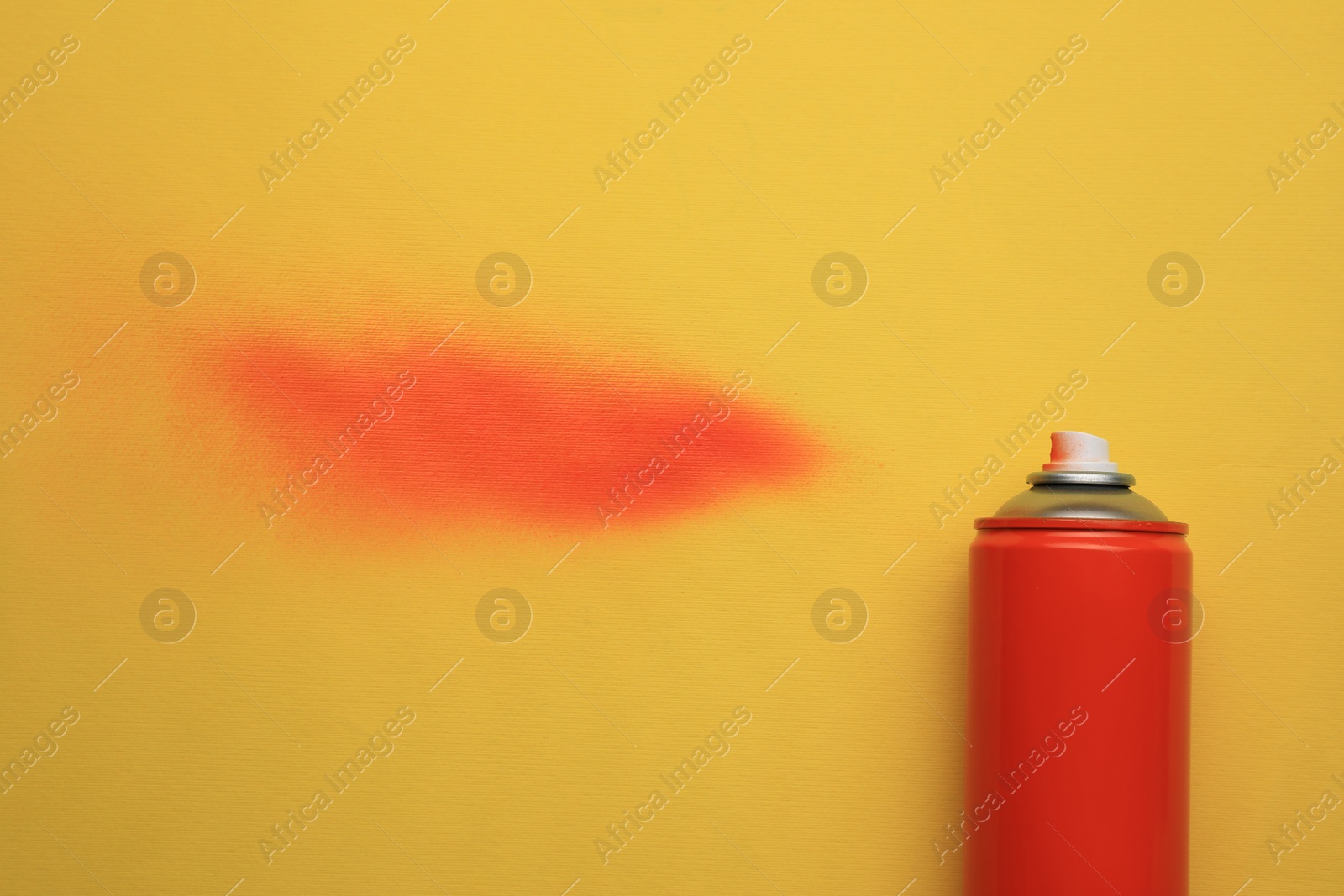 Photo of Can of red graffiti paint and sprayed dye sample on yellow background, top view