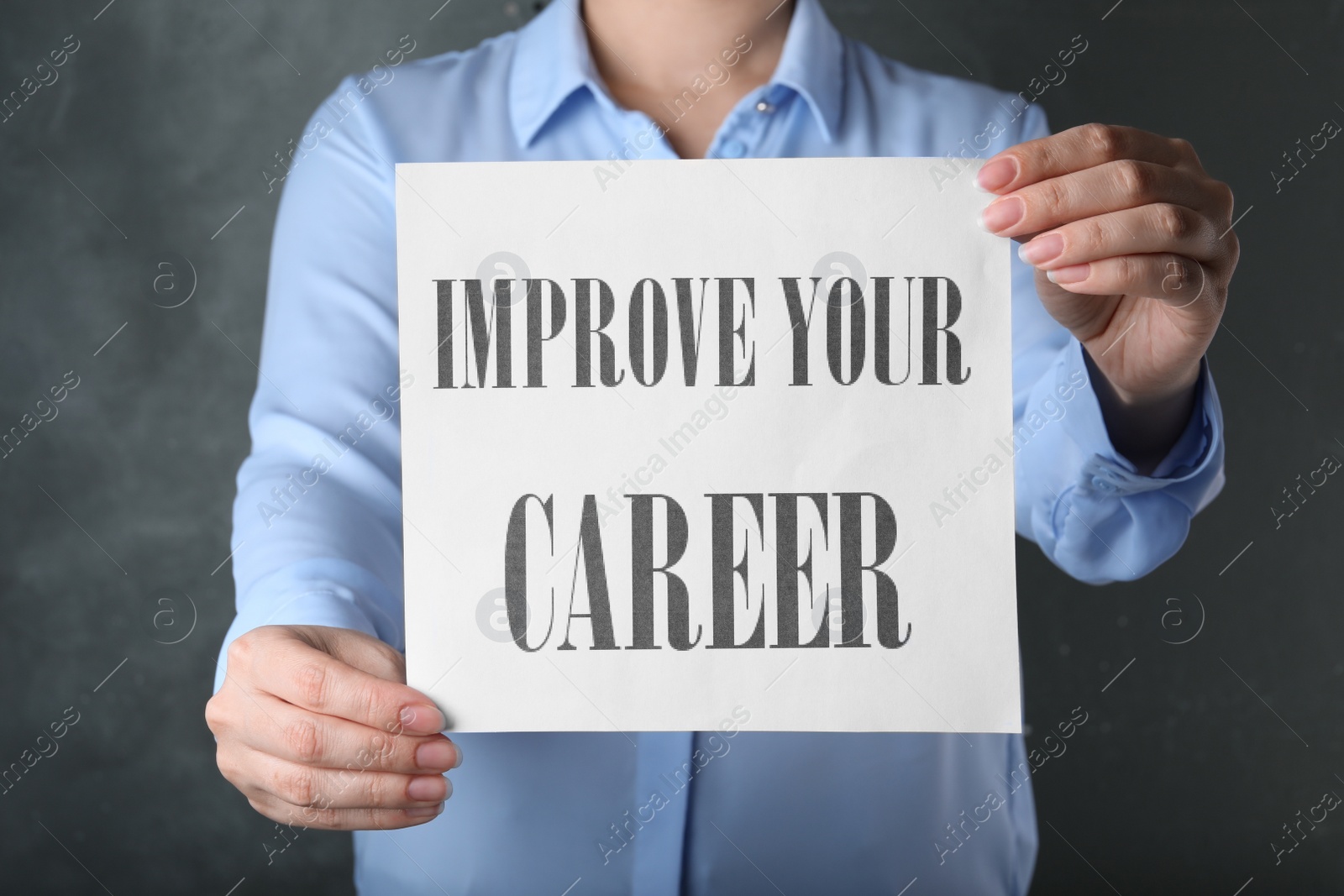 Photo of Woman holding sheet of paper with words IMPROVE YOUR CAREER on grey background, closeup