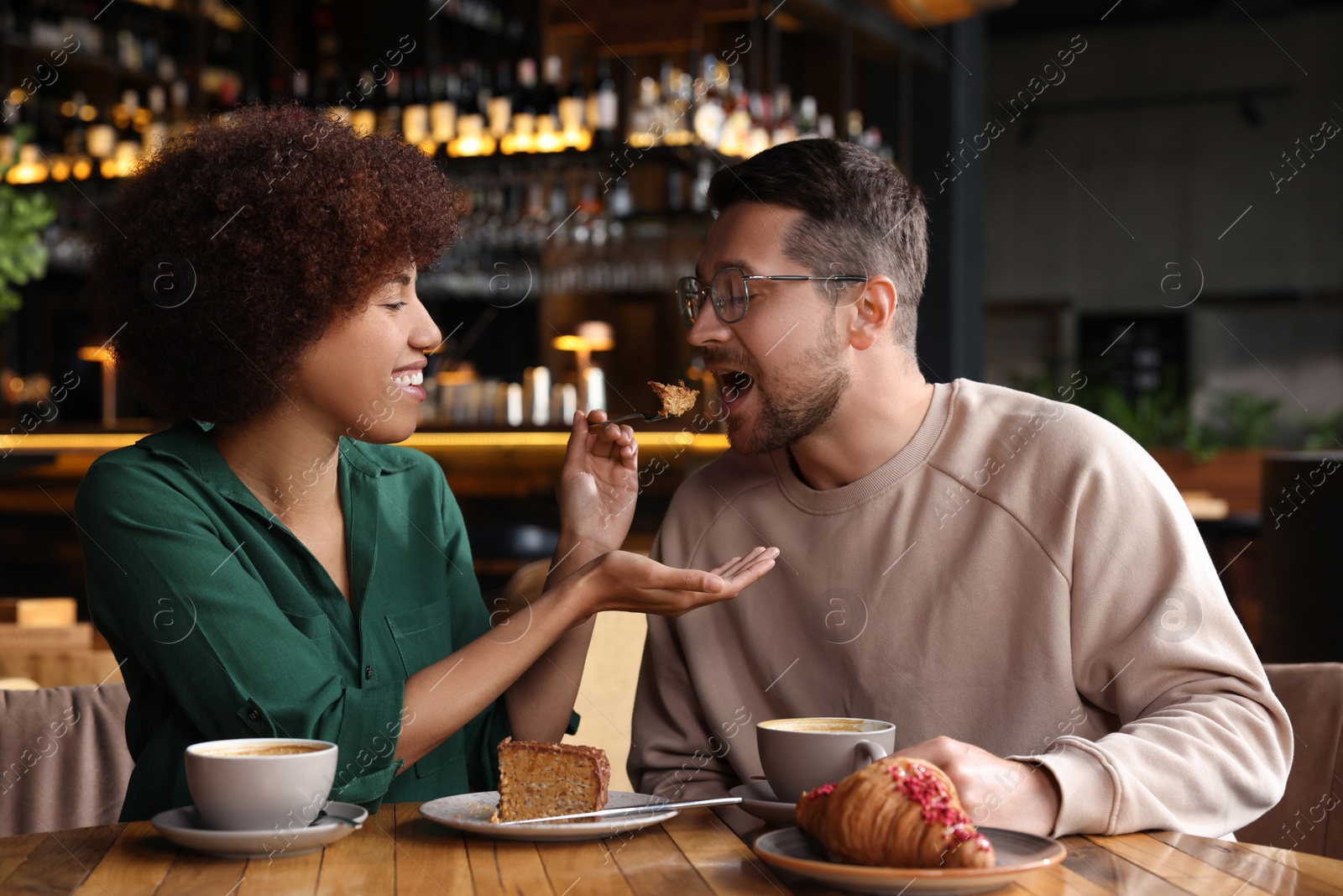 Photo of International dating. Handsome man feeding his girlfriend with cake in cafe