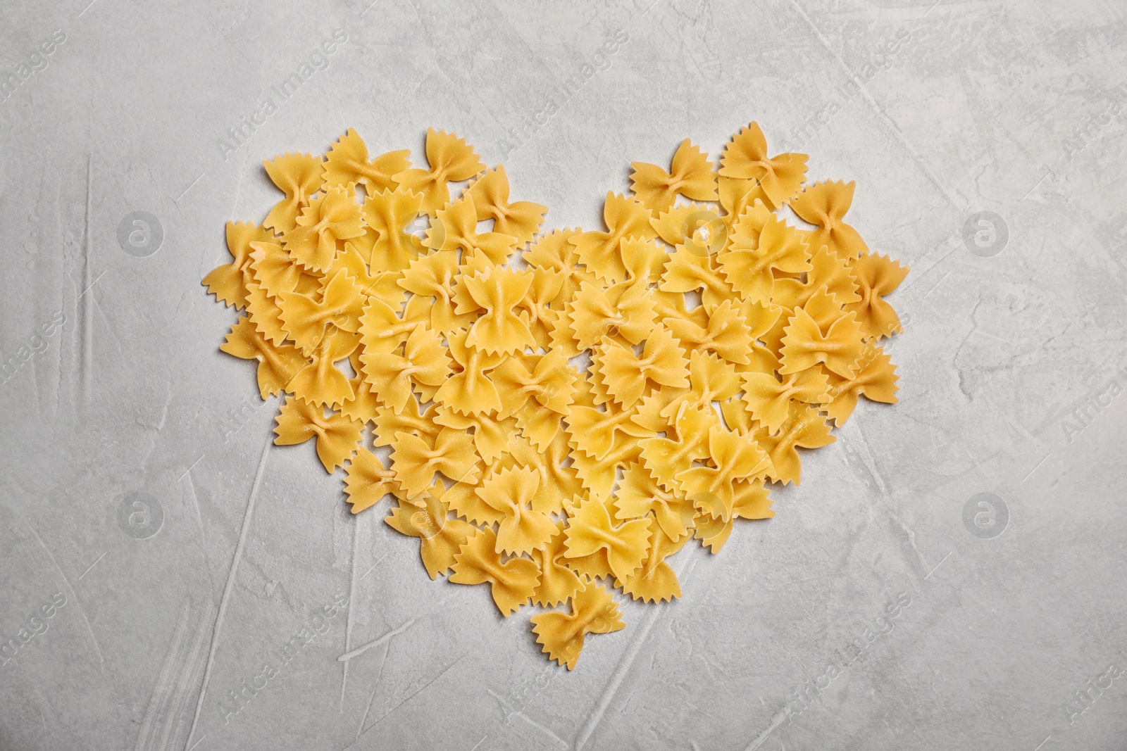 Photo of Heart made of uncooked pasta on grey background, top view