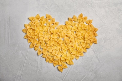 Heart made of uncooked pasta on grey background, top view