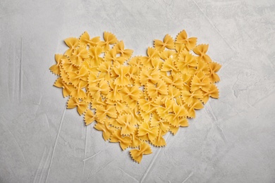 Photo of Heart made of uncooked pasta on grey background, top view