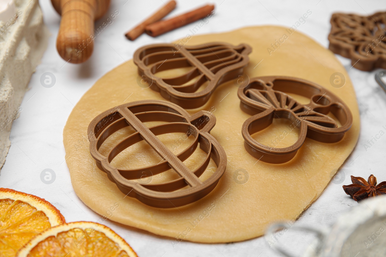 Photo of Cookie cutters, dough and rolling pin on white marble table, closeup