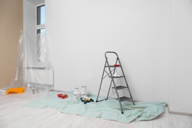 Photo of Metallic folding ladder and painting tools indoors, space for text