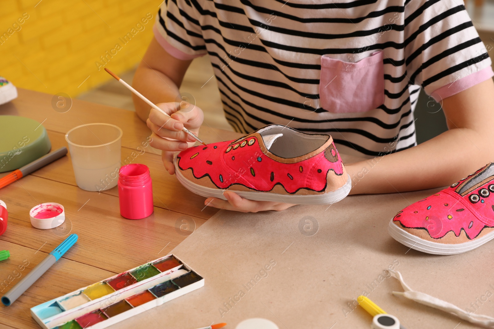 Photo of Woman painting on sneaker at wooden table indoors, closeup. Customized shoes