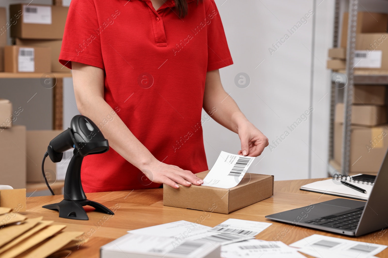 Photo of Parcel packing. Post office worker sticking barcode on box at wooden table indoors, closeup