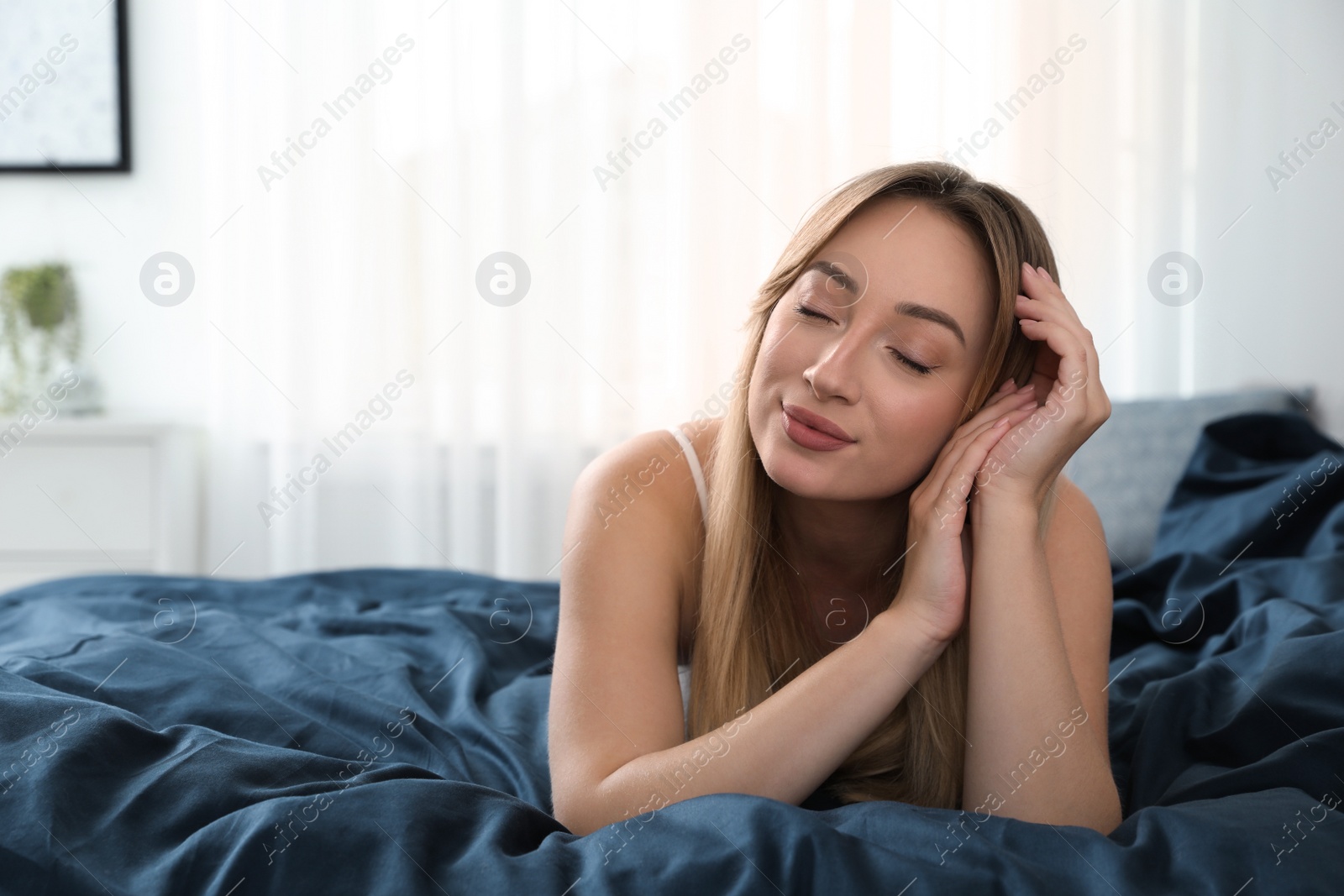 Photo of Young woman lying on comfortable bed with dark blue linens at home